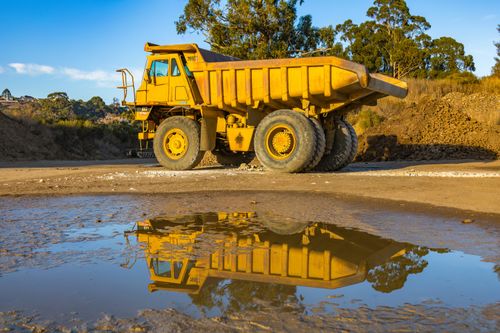 Free Yellow dump truck with reflection in water at a mining site, exhibiting industry machinery. Stock Photo