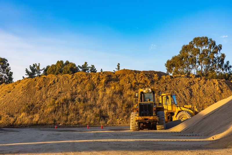 Yellow construction machinery working a dirt pile under blue sky