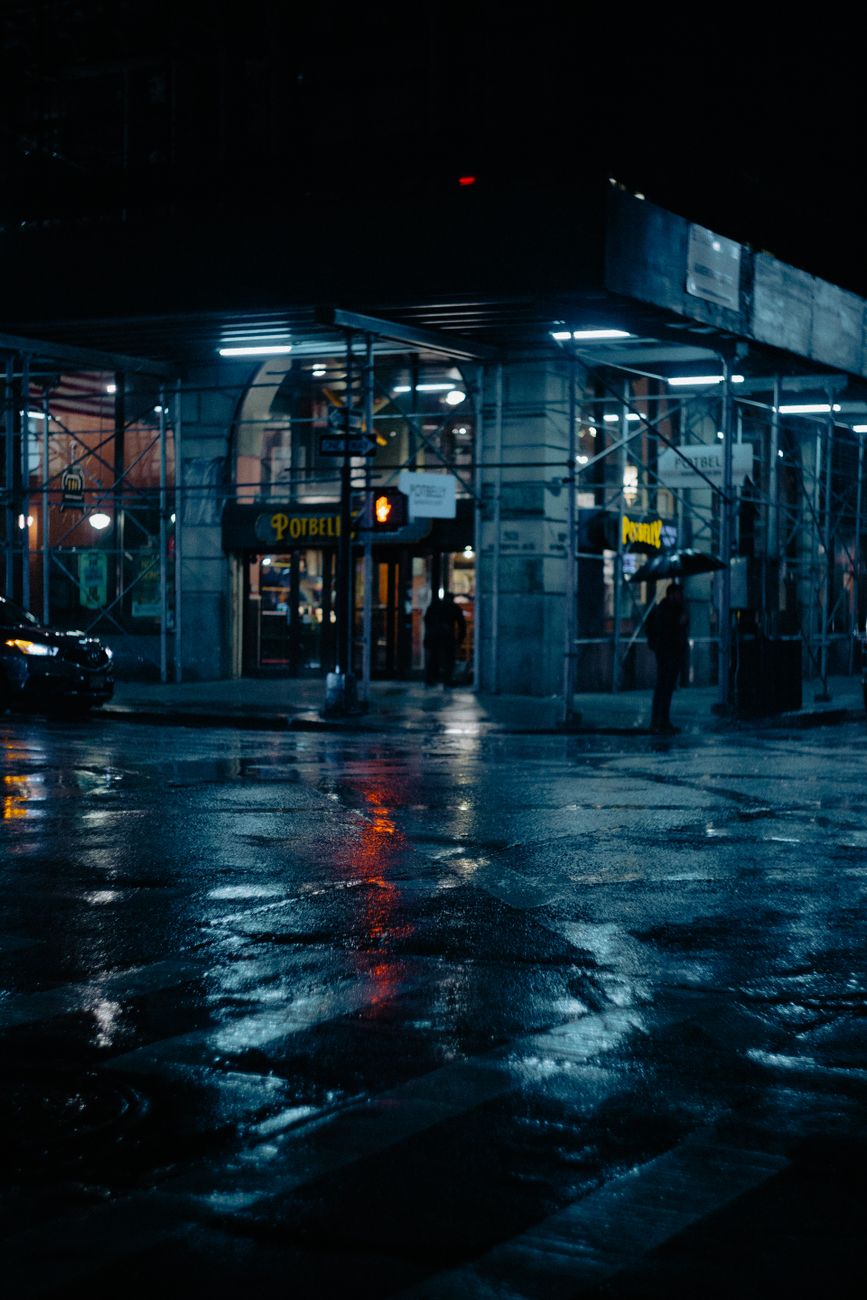 A rainy night street scene in New York City with urban reflections and shadows.