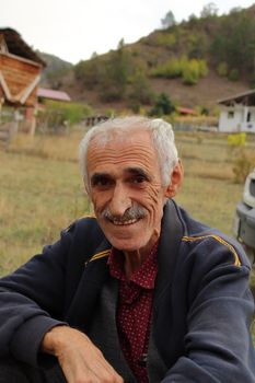 A smiling elderly man poses outdoors in the scenic countryside of Yusufeli, Artvin, Türkiye. - Fotografer Sidoarjo