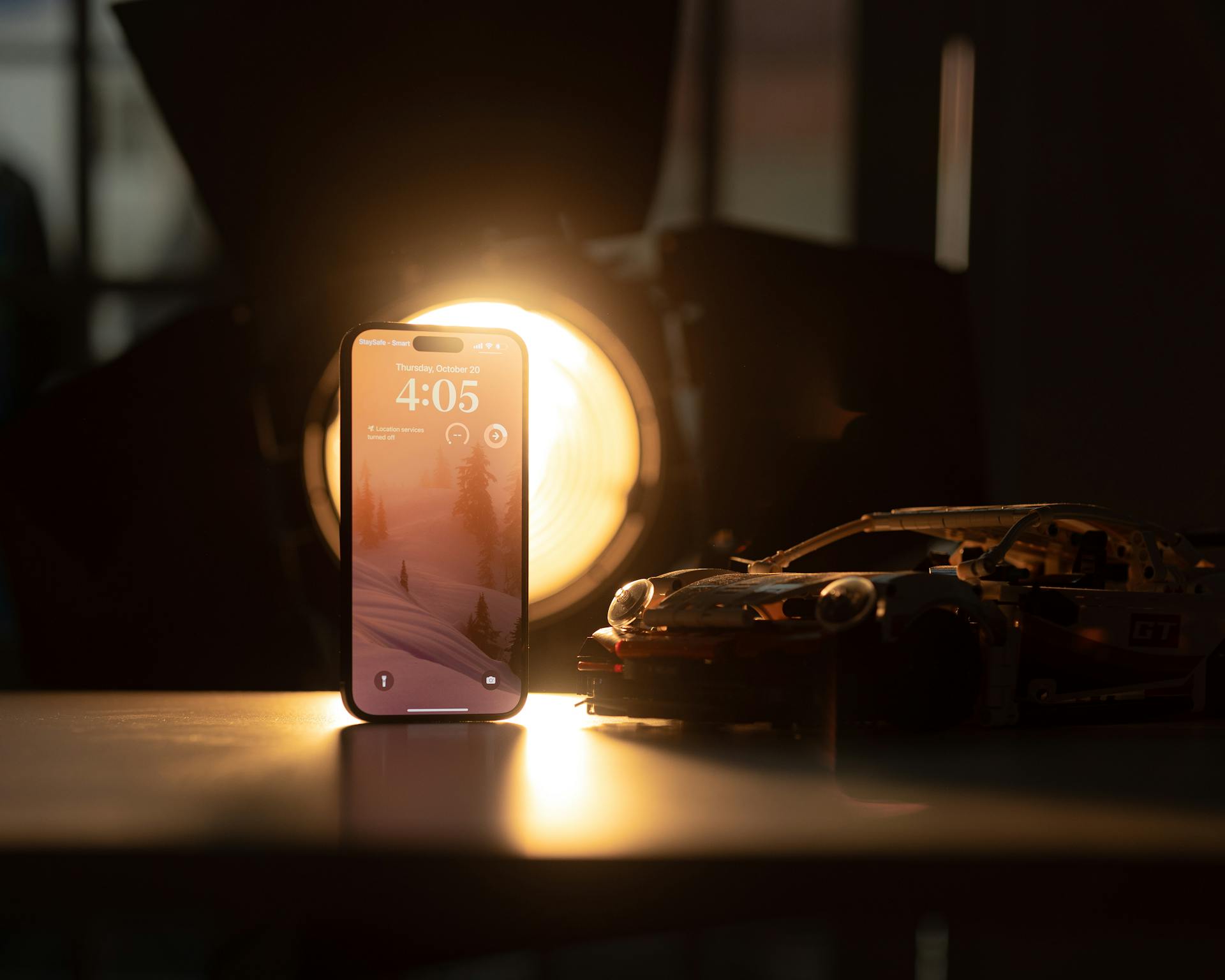 A smartphone and toy car on a desk illuminated by soft lighting, creating a warm ambiance.