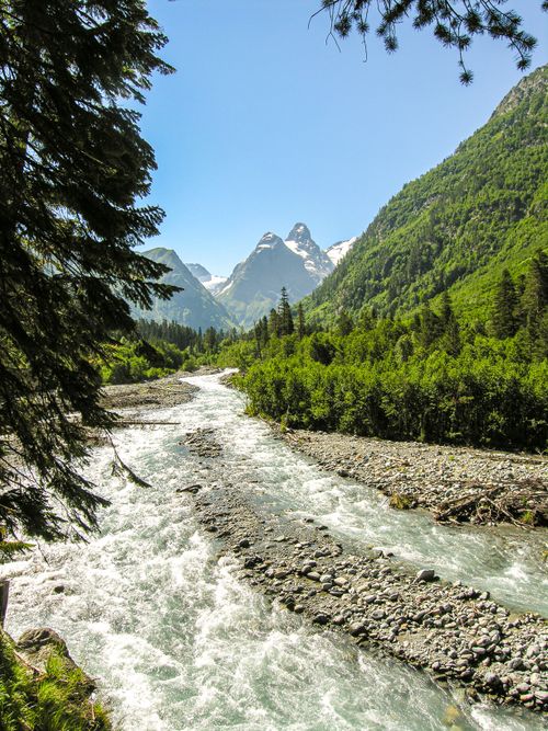 Free Tranquil river flowing through lush green mountain landscape under clear blue sky. Stock Photo