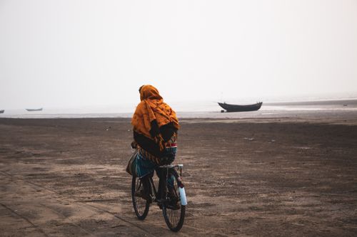 Free Person cycling on a beach at dawn with boats in the distance, creating a serene scene. Stock Photo