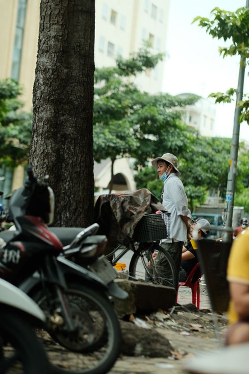 Free A street vendor with a bicycle stands by a busy urban roadside, showcasing daily life. Stock Photo