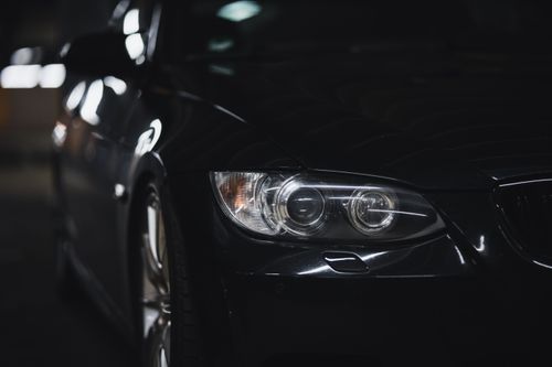 Free A sleek black sedan with a shining headlight in a dimly lit setting, emphasizing modern automotive design. Stock Photo