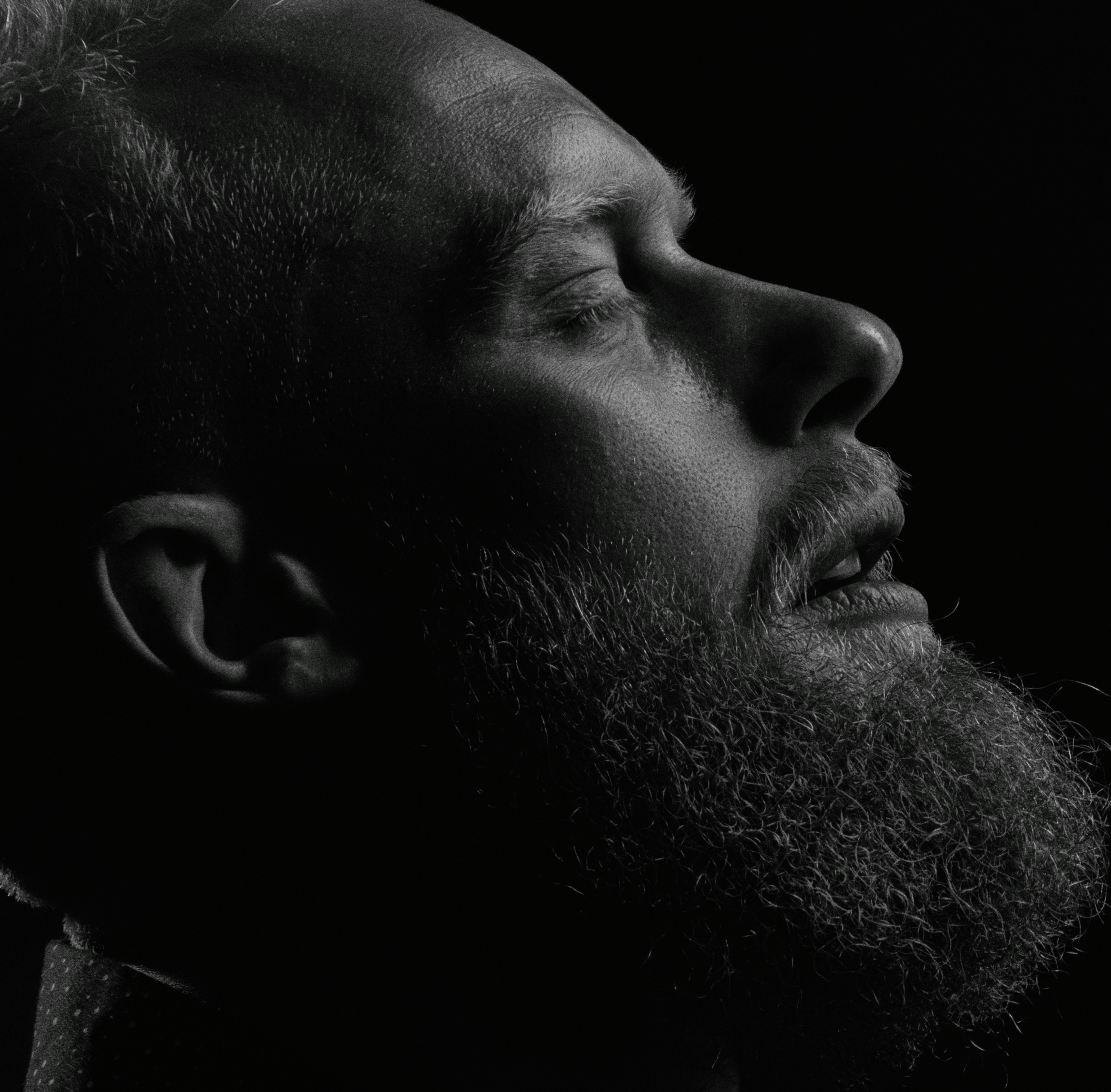Black and white close-up of a bearded man in side view, capturing emotion and texture.