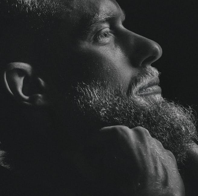 Side profile of a thoughtful bearded man in grayscale lighting.