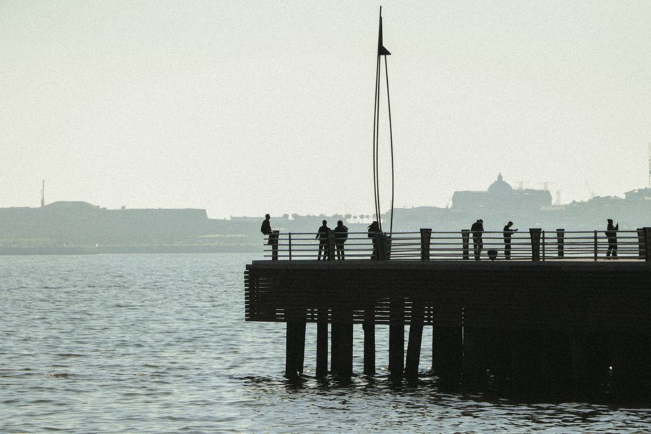 Silhouettes of people standing on a pier in Baku with a city's skyline in the background.