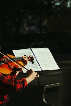 A violinist plays passionately from a music sheet in an outdoor setting, capturing the essence of live music.