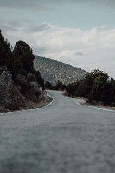 A tranquil curved road stretches through a picturesque mountain landscape under a cloudy sky.