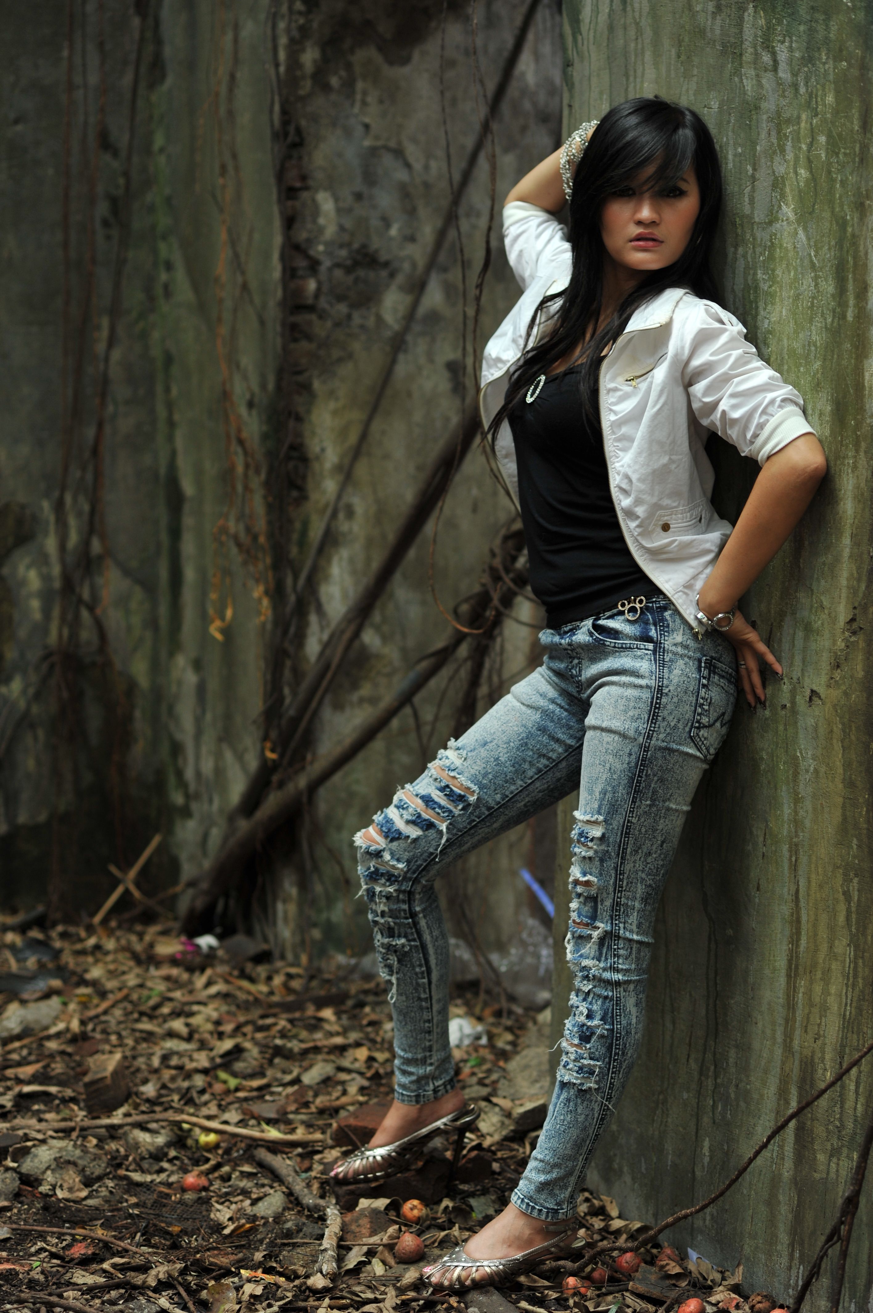 Asian woman in trendy attire confidently posing against an urban backdrop.