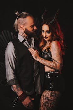 Intimate portrait of a stylish gothic couple with tattoos and horns in a dark setting.