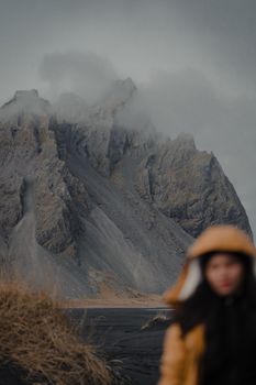 A woman in winter attire overlooks a foggy mountain landscape, creating a dramatic scene.