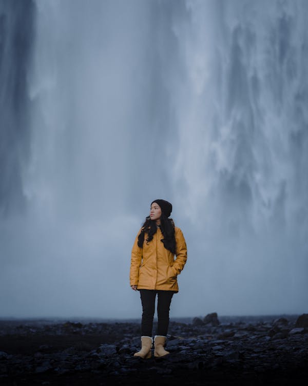 Woman in Brown Jacket Standing on Rock Near Water Falls