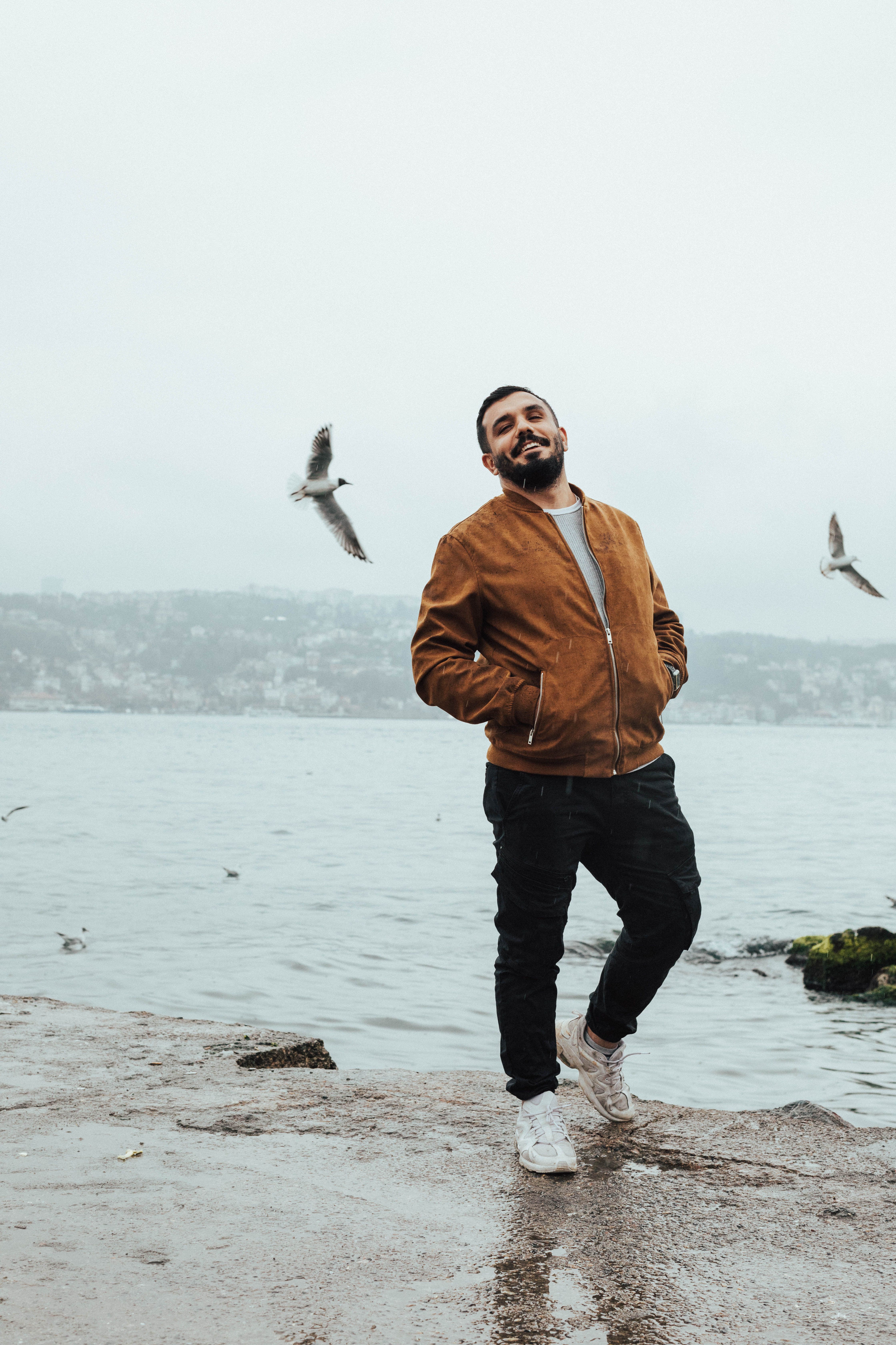 Smiling man in a jacket walks by the sea with seagulls in Turkey.