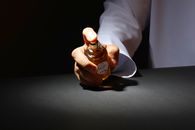 A hand elegantly holding a perfume bottle against a dark backdrop, highlighting luxury fragrance.
