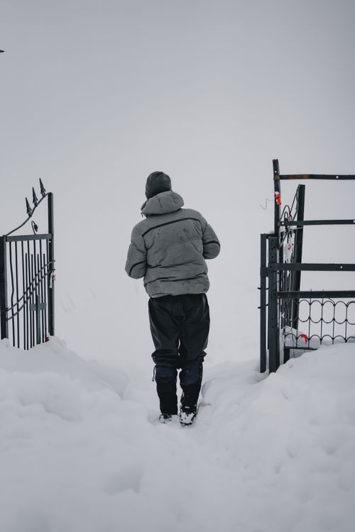 Free Adult walking through a snow-covered gate during heavy winter snowfall, back view. Stock Photo