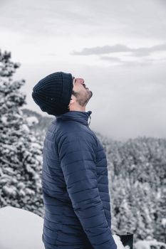 Side profile of a man in a winter jacket and beanie enjoying a snowy forest view.