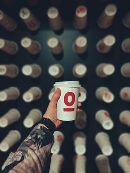 Hand holding a coffee cup with a red number pattern, creating a dynamic backdrop in an indoor setting.