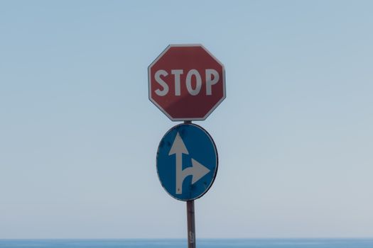 Stop sign with directional arrows at Lido di Noto, Sicily with sky backdrop.