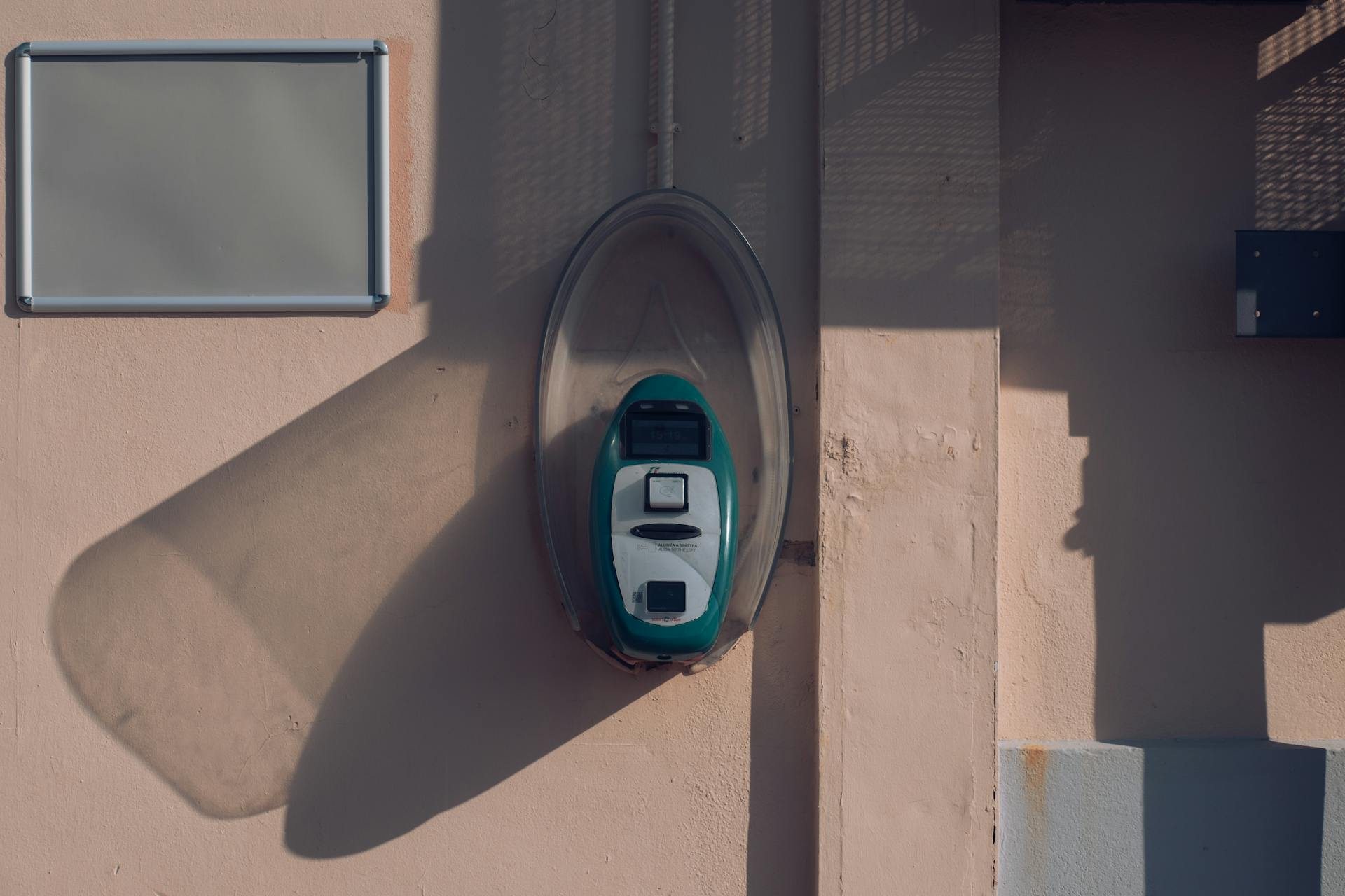 Ticket validator mounted on a wall in Avola, Sicily, casting a shadow in the afternoon light.