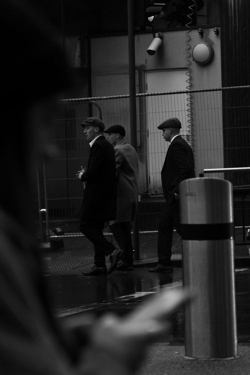 Free A black and white photo of three men in coats and flat caps walking on a wet city street. Stock Photo