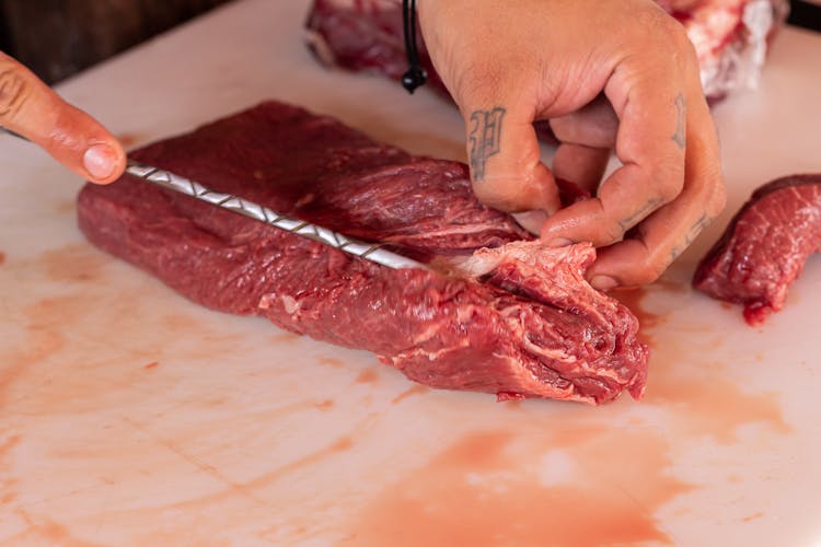 A Person Slicing Raw Meat On The Table