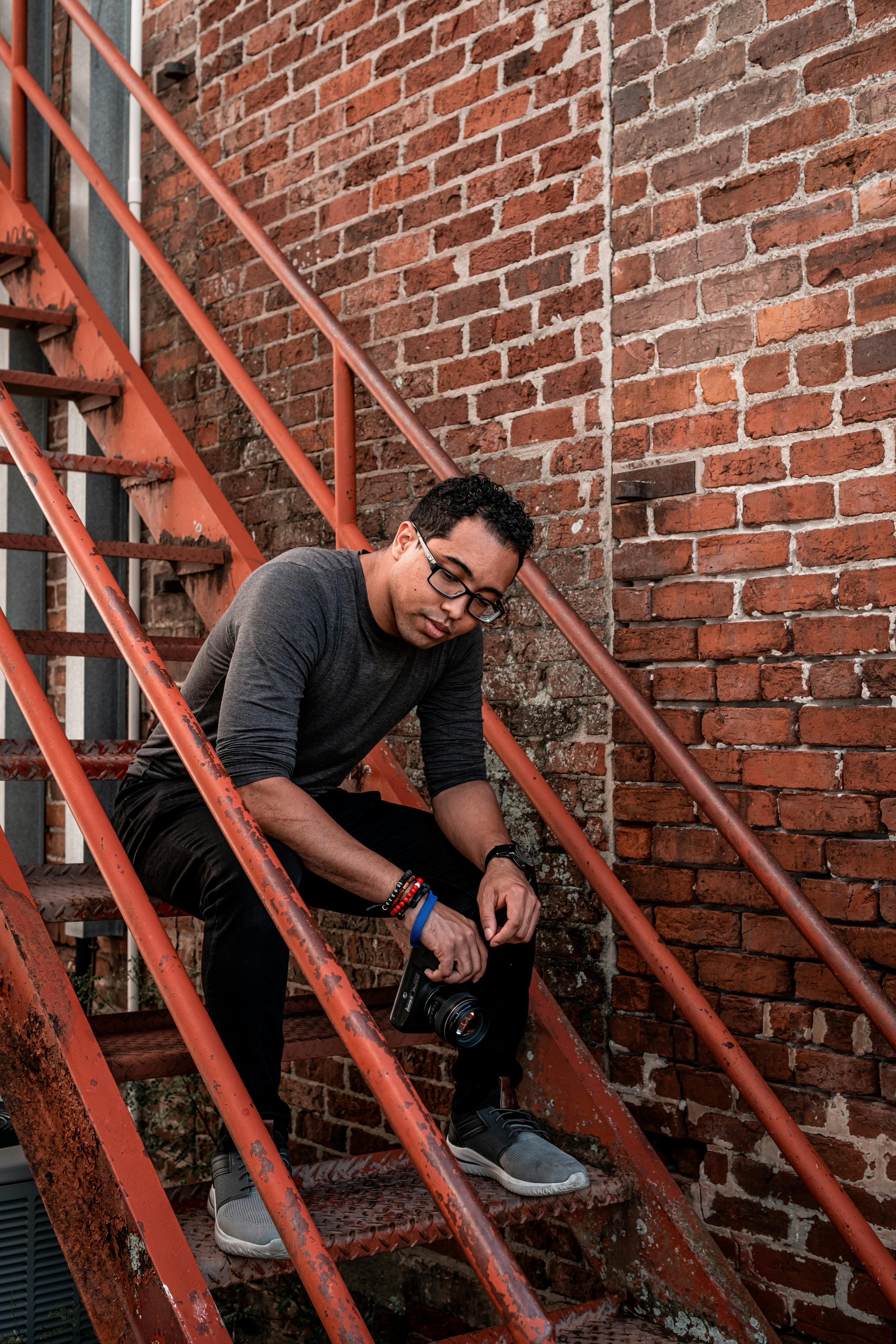 man in gray crew neck t shirt and brown pants sitting on brown wooden staircase