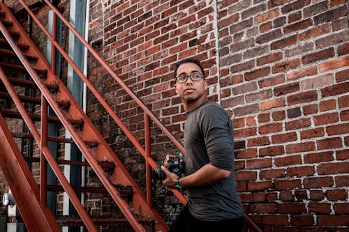 Man in Black Long Sleeve Shirt Standing on Metal Staircase Holding Camera