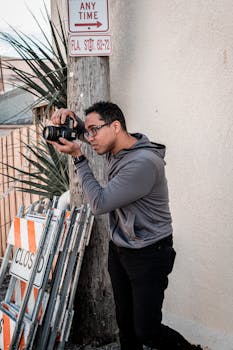 Male photographer using a camera outdoors near a closed sign on a sunny day.