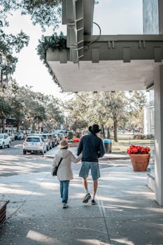 A couple strolls through a sunlit city park, showcasing fall's charm.