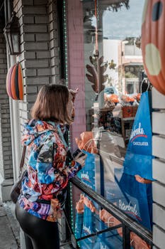 Adult woman browsing a chocolaterie storefront with fall decorations on an urban street.