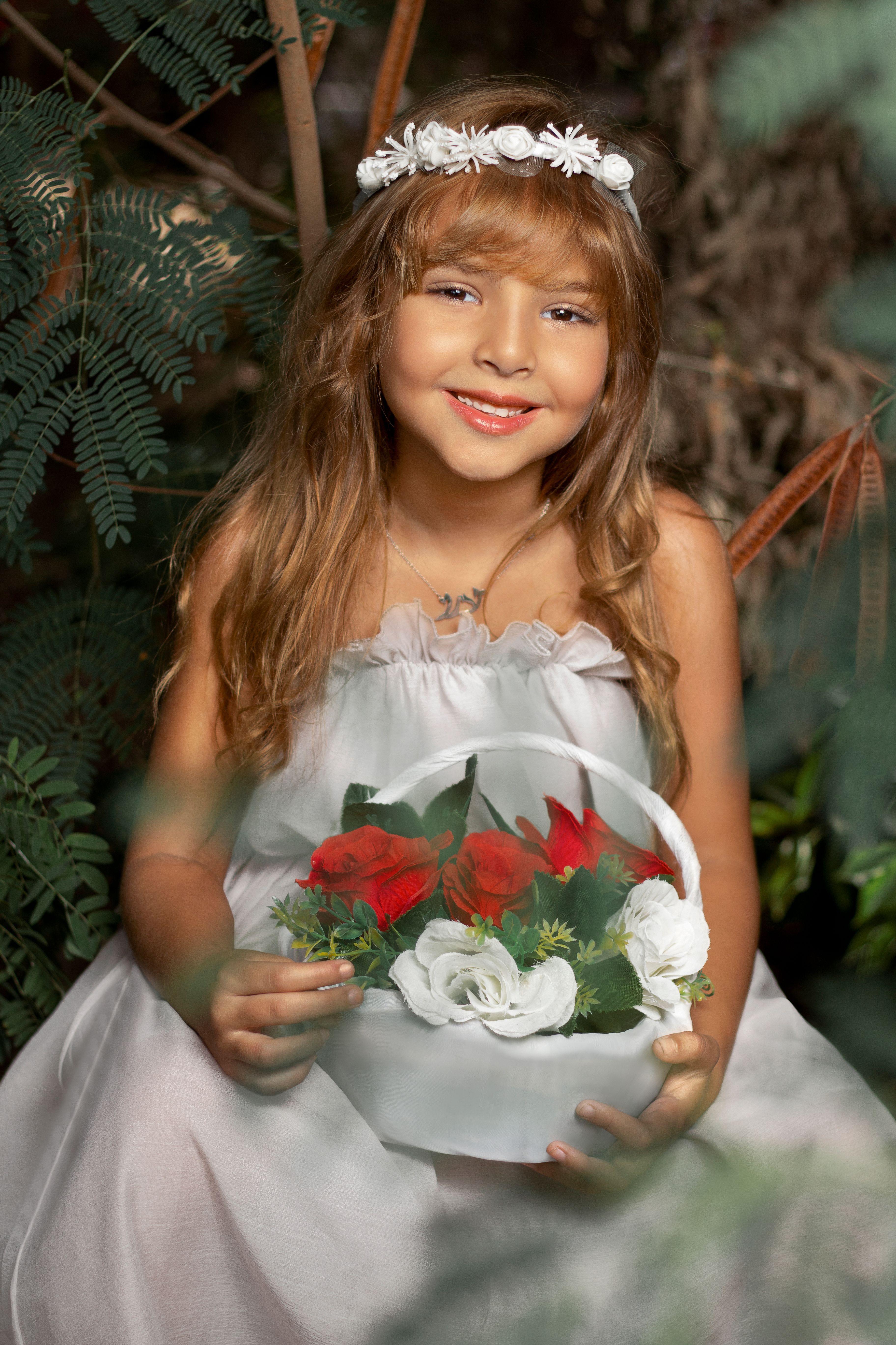 Smiling young girl in white dress holds a colorful bouquet outdoors.