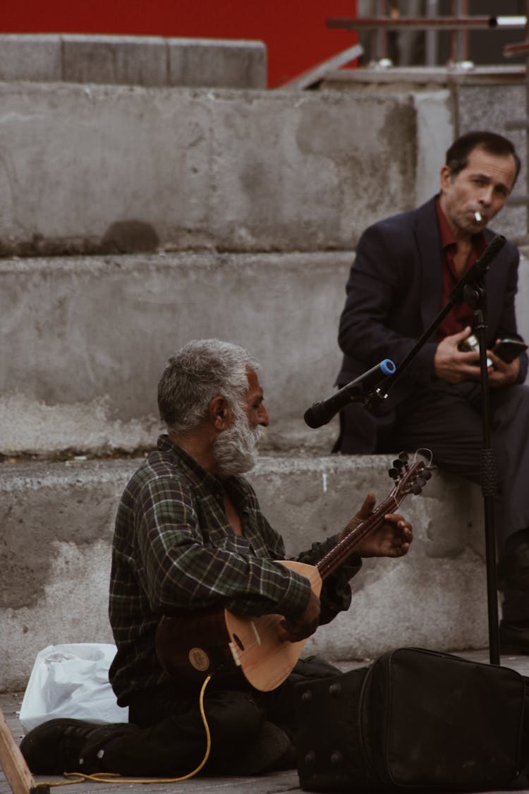 An Elderly Man Playing A String Instrument In The Street