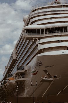 Low angle view of a massive cruise ship docked under a cloudy sky, ideal for travel and transportation themes.