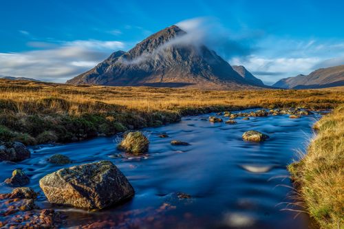 Free Scenic view of a mountain with a flowing creek under a bright blue sky. Captivating nature scene. Stock Photo