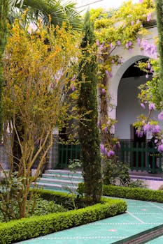 A lush, formal Parisian courtyard garden with flowering plants and a grand archway.