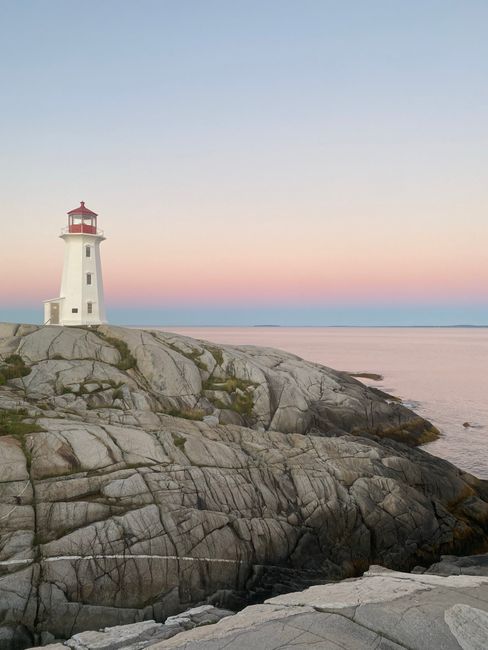 Serene coastal scene of a lighthouse standing on rocky shoreline at sunset, ideal for travel inspiration.