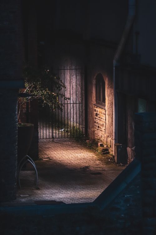 Free Eerie alleyway with dim lighting casting creepy shadows on brick walls and a wrought iron gate. Stock Photo