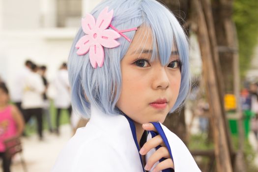 Close-up portrait of a young woman in cosplay with blue hair and floral accessory outdoors.