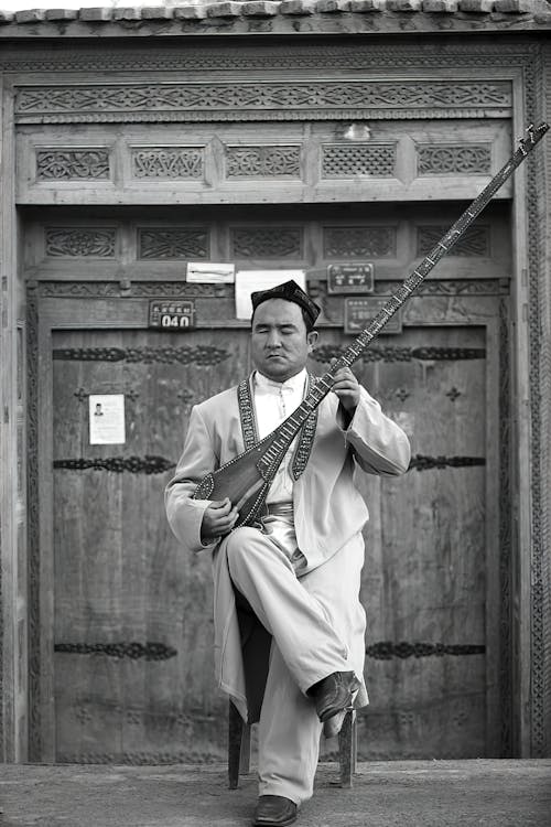 Black and White Photo of Man Sitting in front of Entrance with Musical Instrument