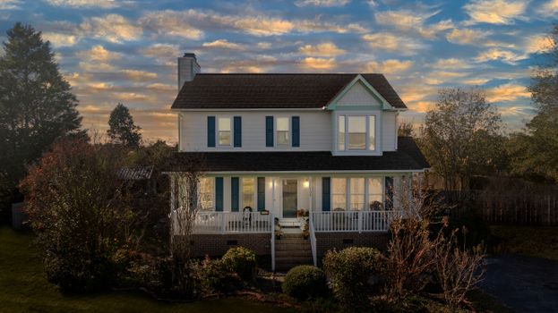 A picturesque two-story suburban house with a cozy front porch and beautiful sunset sky.