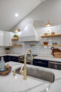A contemporary luxury kitchen with gold fixtures, navy cabinets, and an elegant white backsplash.
