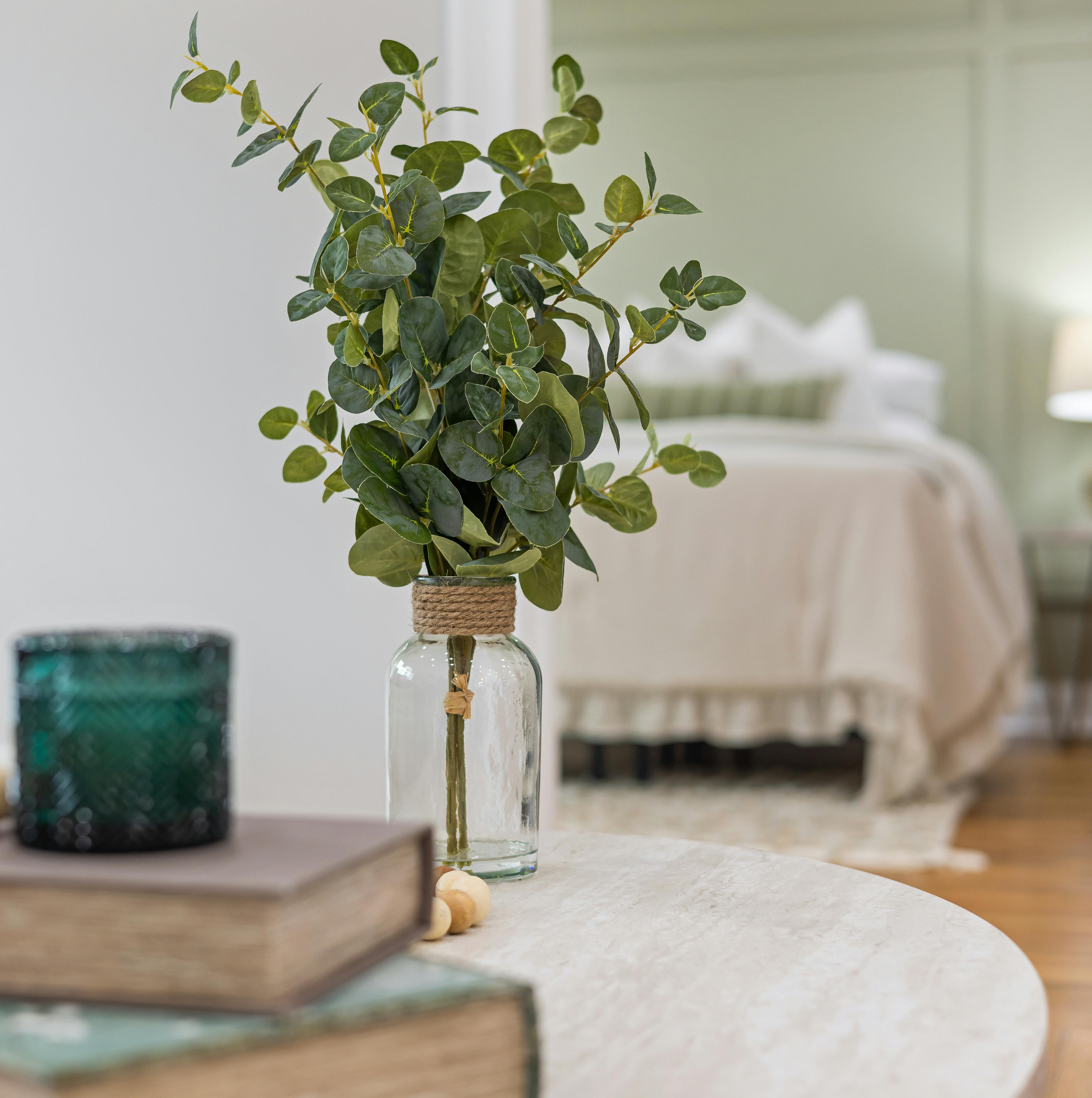 Eucalyptus in a glass vase on a table adds a fresh touch to a cozy bedroom setup.