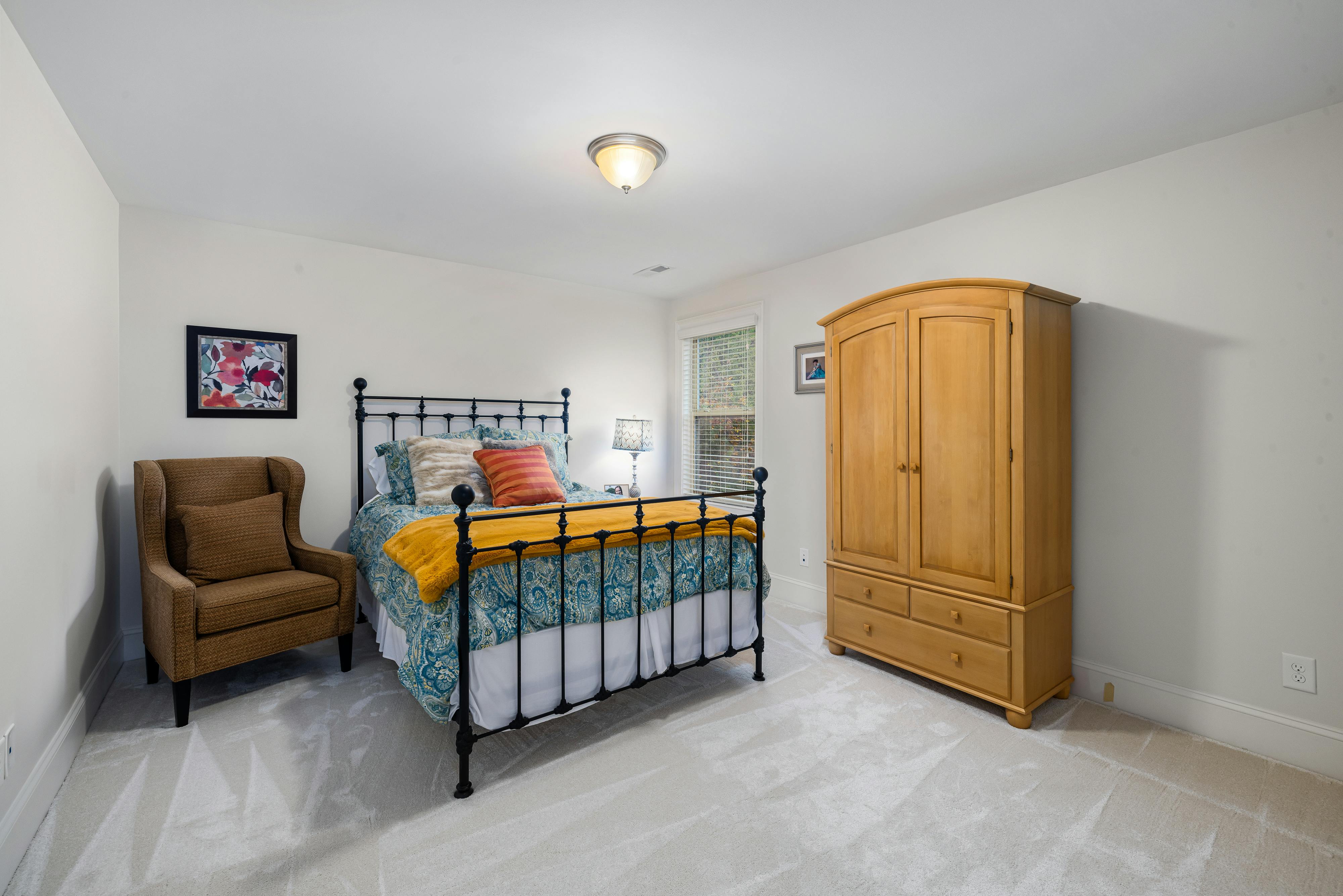 Inviting bedroom design featuring a metal bed frame, wooden wardrobe, and accent chair, perfect for modern interiors.