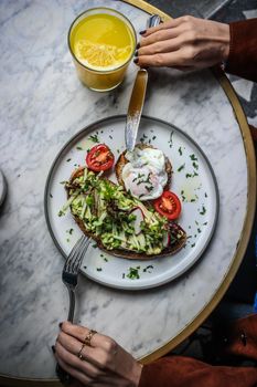 Top view of avocado toast with poached egg, tomato, and orange juice on a marble table.
