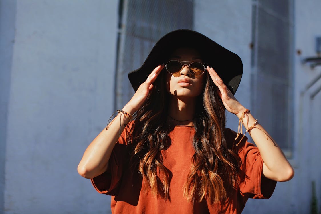 Женщина в коричневой рубашке и шляпе от солнца у белой стены