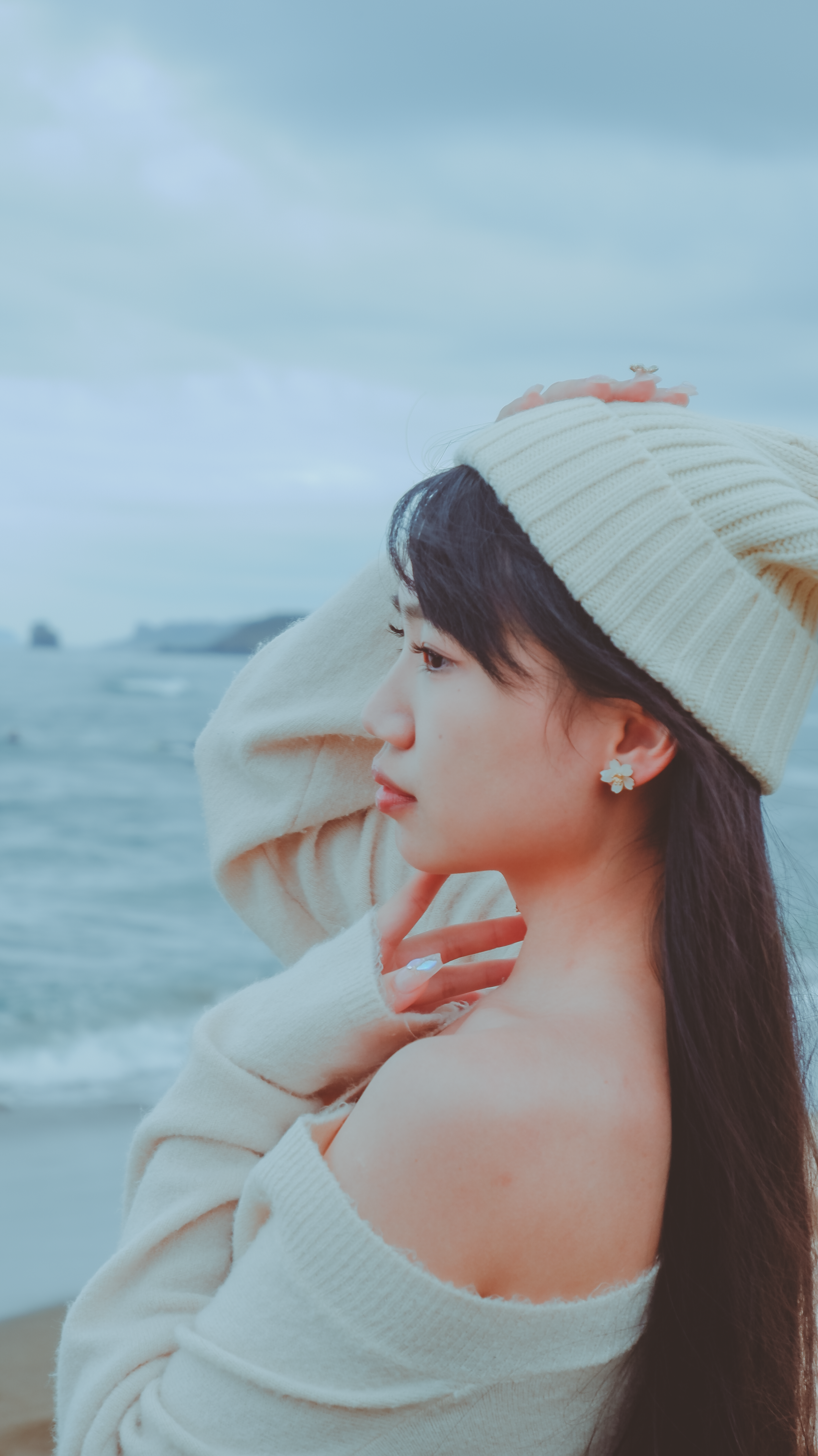 A thoughtful woman in knitwear poses by the ocean, expressing tranquility and style.