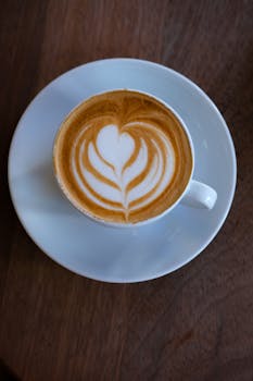 Top view of a cappuccino with intricate latte art on a wooden table.
