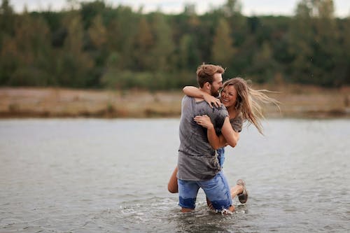 무료 물의 몸에 서있는 동안 웃는 여자를 껴 안고 남자 스톡 사진